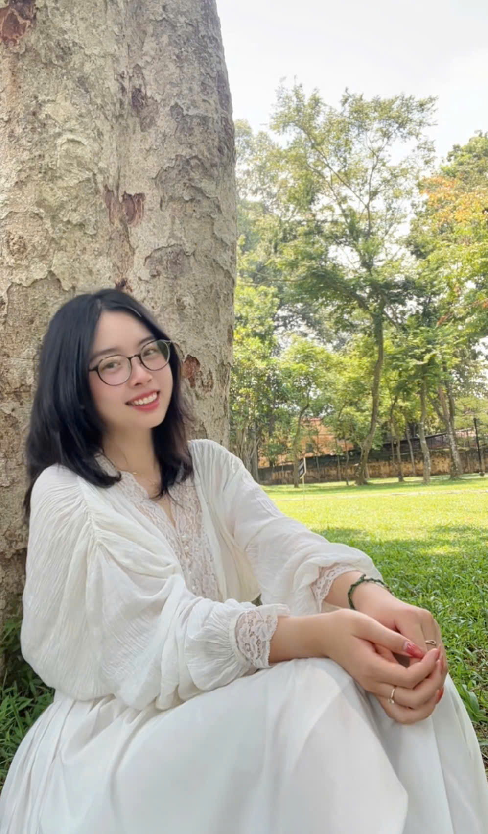 Tú Xương ngồi tựa gốc cây, mặc áo trắng, mỉm cười